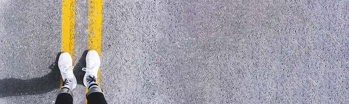 someones feet standing on the yellow lines of a road